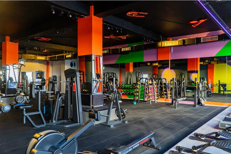 Today Living Club fitness salonu geniş açı: kablo istasyonları, ağırlık makineleri ve kürek makinesi, turuncu kolonlar ve neon tavan
