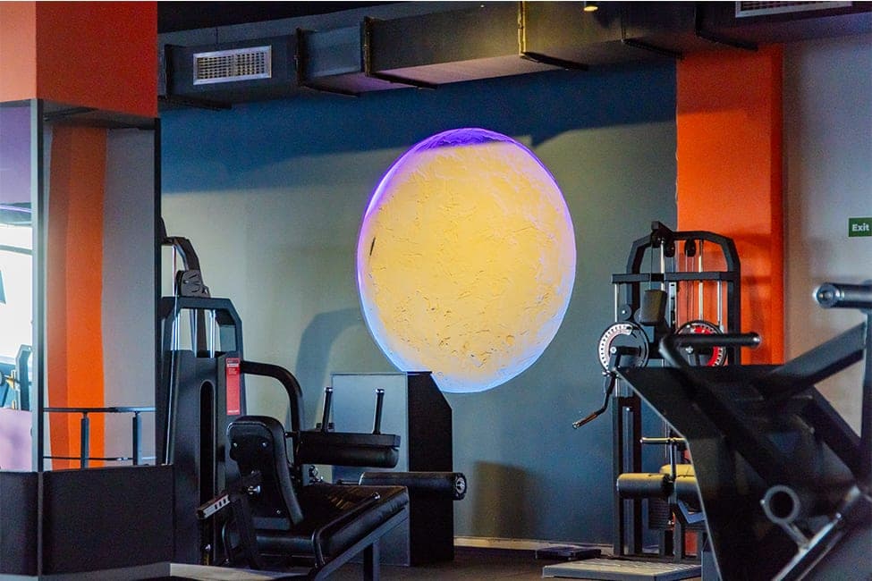 Today Living Club fitness alanında turuncu kolonlar arasında ışıklı ay lamba ve ağırlık makineleri