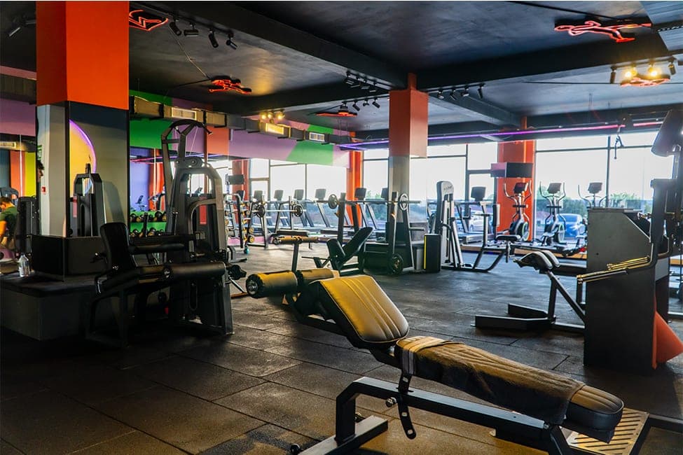 Today Living Club fitness salonu: ön planda bench, arkada koşu bantları ve eliptikler, turuncu kolonlar ve renkli duvarlar