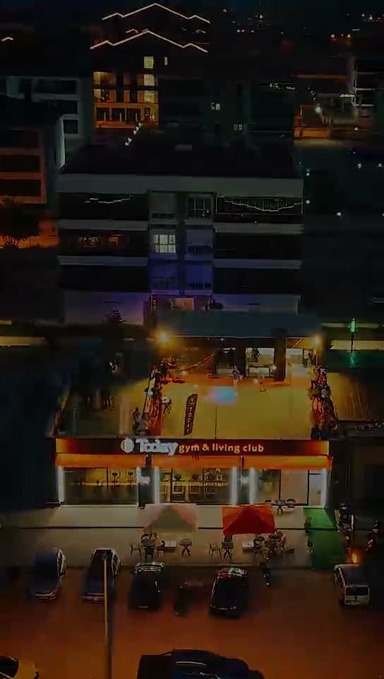 Today gym & living club binasının gece görünümü: ışıklı turuncu tabela ve önündeki park alanı