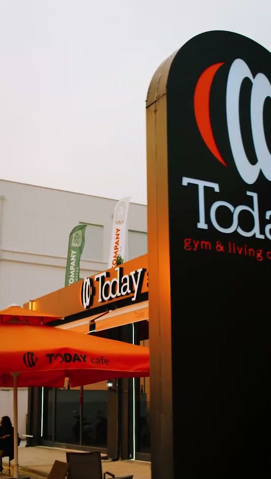 Gün batımında Today gym & living club totem tabelası, ışıklı cephe ve Today Cafe şemsiyeleri