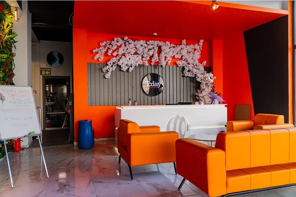 Today Living Club resepsiyonu: turuncu duvarlar, beyaz karşılama bankosu, Today logosu ve turuncu deri koltuklar